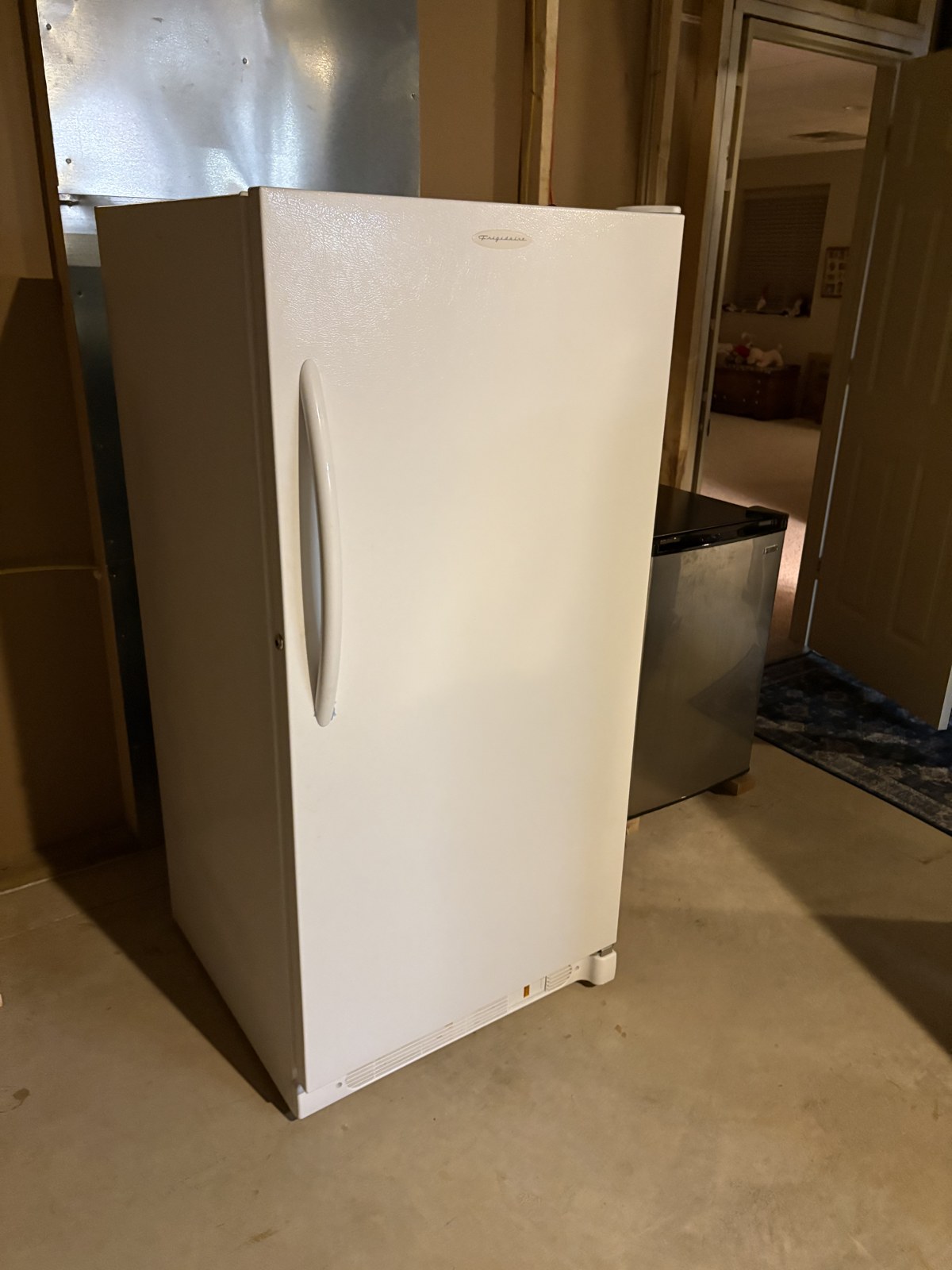 White upright Frigidaire freezer standing in a basement before removal